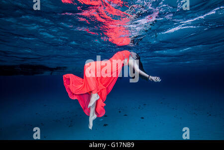 Woman in red floating near surface of ocean Stock Photo