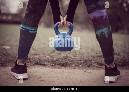 Rear view of womans low section, open legged holding kettle bell Stock Photo