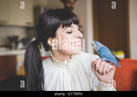 Young woman smiling at pet bird indoors Stock Photo