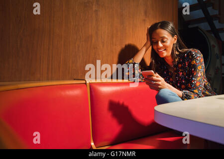 Woman sitting in wood panelled booth looking down at smartphone smiling Stock Photo