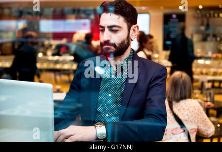 Businessman sitting in cafe window seat typing on laptop Stock Photo