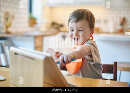Baby boy sitting at table pointing at digital tablet Stock Photo