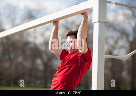Young man doing pull ups on playing field goal post Stock Photo