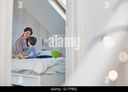 Pregnant mother sitting on bed with baby boy holding book face to face smiling Stock Photo