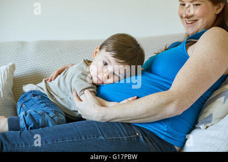 Baby boy lying on mothers pregnant stomach looking at camera Stock Photo