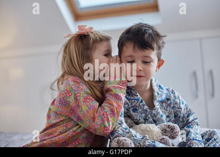 Girl whispering into boy's ear in loft room Stock Photo