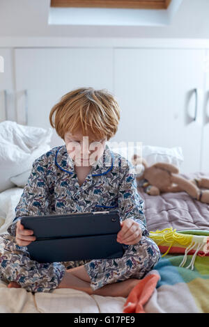 Boy in pyjamas using digital tablet in bed Stock Photo