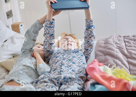 Children in pyjamas using digital tablet in bed Stock Photo