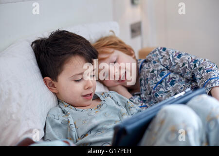 Boys in pyjamas using digital tablet in bed Stock Photo