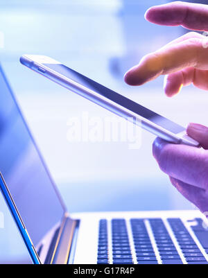 Man operating a touch screen mobile phone with a laptop in the background. Stock Photo