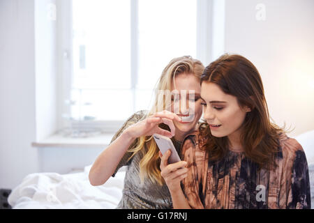 Two young women sitting on bed reading smartphone texts Stock Photo