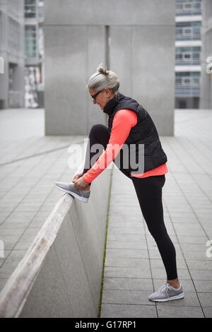 Mature woman training in city, tying trainer laces Stock Photo