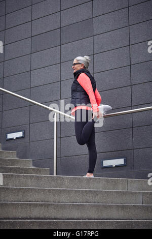 Mature woman training in city, stretching legs on stairway Stock Photo