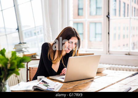 Young woman in city apartment laughing whilst working on laptop Stock Photo