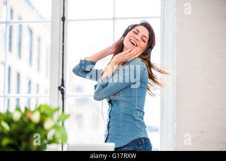 Young woman dancing to headphone music in front of city apartment window Stock Photo