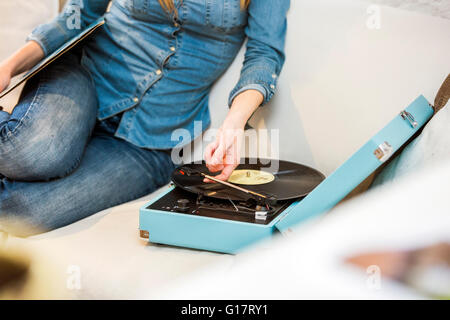 Cropped shot of young woman sitting on sofa listening to vintage record player