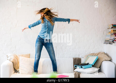 Young woman standing on sofa dancing and shaking her hair Stock Photo