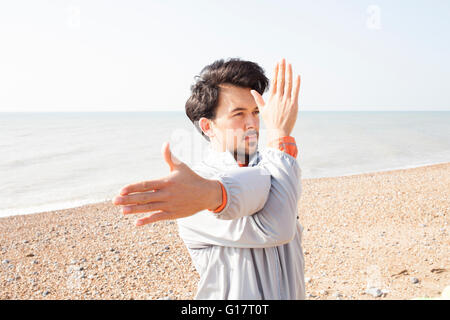 Young man warm up training, stretching arms on Brighton beach