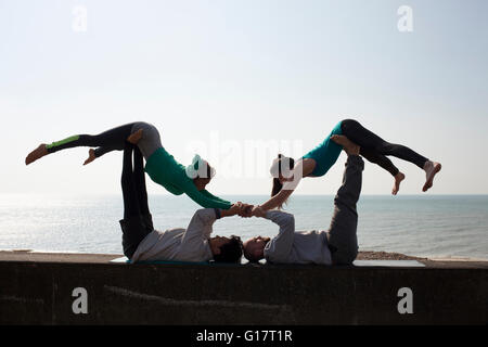 Silhouetted men and women practicing acrobatic yoga on wall at Brighton beach Stock Photo