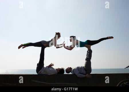Symmetrical silhouetted men and women practicing acrobatic yoga on wall at Brighton beach Stock Photo