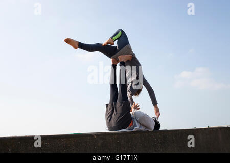 Man and woman practicing acrobatic yoga on wall against blue sky Stock Photo
