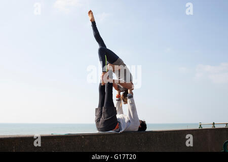 Man and woman practicing acrobatic yoga on wall at Brighton beach Stock Photo