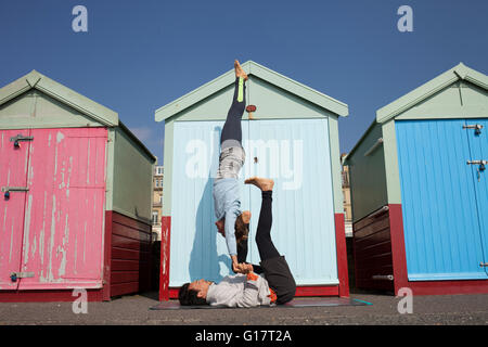 Man and woman practicing acrobatic yoga in front of beach huts at Brighton beach Stock Photo