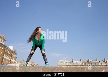 Exhausted female runner standing on wall taking a break Stock Photo