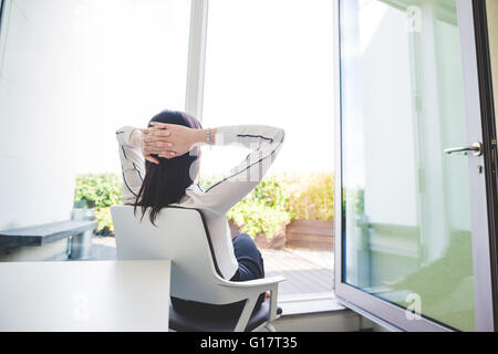 Young businesswoman relaxing in office looking out of patio doors Stock Photo