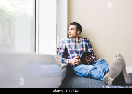 Young male sitting on office floor looking through window Stock Photo