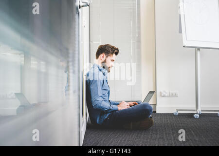 Young male sitting on office floor using laptop Stock Photo