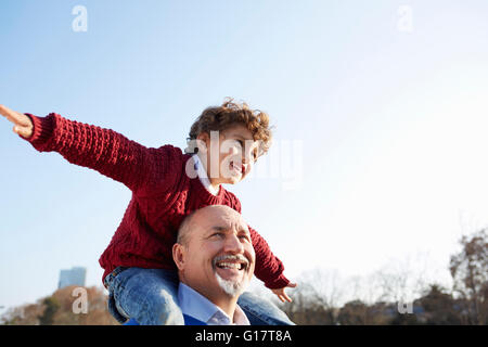 Grandson sitting on grandfathers shoulders, arms out smiling Stock Photo