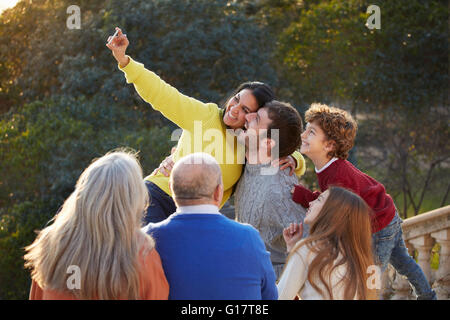Mid adult woman and family using smartphone to take selfie in park Stock Photo
