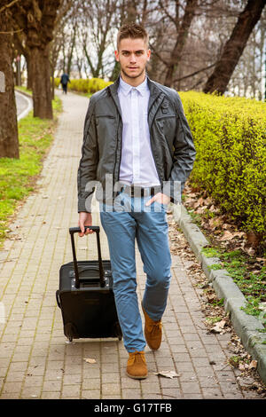 Young man in trendy clothes with baggage standing on pavement while looking at camera Stock Photo