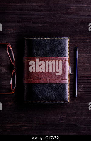 Book, eyeglasses and pen laid on old wooden table Stock Photo