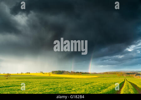 Dark Rainy Clouds and a Rainbow over British Spring Farm Land Stock Photo