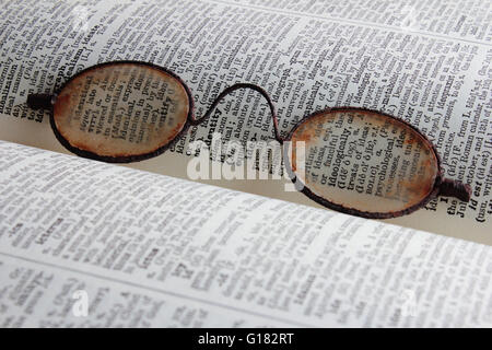 Antique reading glasses resting on an open dictionary page. Stock Photo