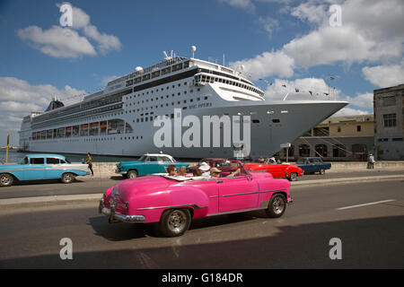 An old restored 1950's American car used as a taxi driving past a docked cruise ship in Havana Vieja Cuba Stock Photo