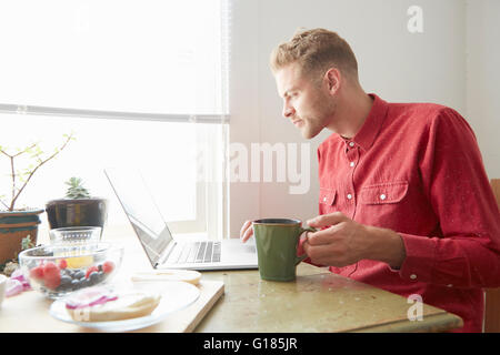 Young man sitting at dining table using laptop Stock Photo