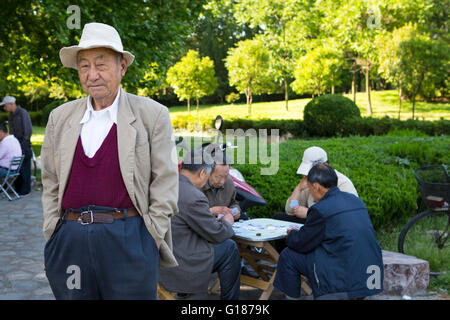 Portrait of a Chinese man with a white hat in a park with people playing cards in the background on a sunny day Stock Photo