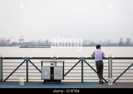 Chinese man looking at the view on the Yangtze river with a ship and shipyards in Nanjing, China Stock Photo