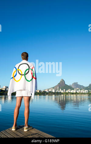 RIO DE JANEIRO - MARCH 04, 2015: Man stands draped in Olympic flag at Lagoa Rodrigo de Freitas Lagoon reflecting Two Brothers Mt Stock Photo