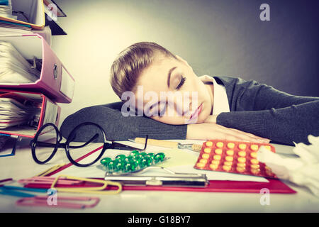 Health concept at business work. Tired overworked young businesswoman secretary manager. Sick ill young female sleeping at workplace. Stock Photo