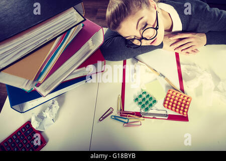 Health concept at business work. Tired overworked young businesswoman secretary manager. Sick ill young female sleeping at workplace. Stock Photo