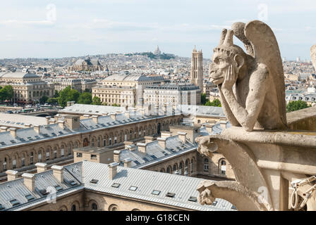 A spitting gargoyle sits on top of Notre Dame surveying the Parisian cityscape below. Stock Photo