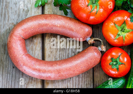 Beef sausage on wooden background with parsley, cucumber and tomato. Flat lay Stock Photo