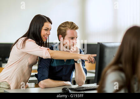 Young beautiful woman helping classmate understand by pointing at the computer screen Stock Photo