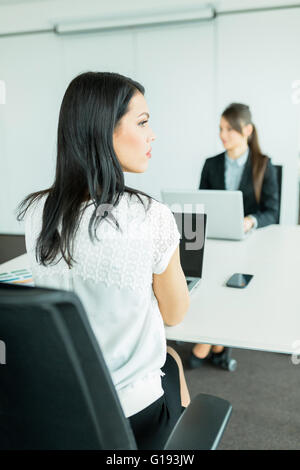 Beautiful young businesswoman looking away from the desk in an office while her colleague works on a laptop Stock Photo