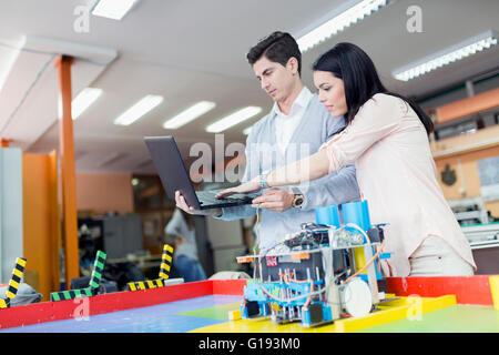 Two smart students programming a robot on a laptop Stock Photo