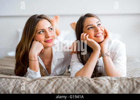 Two beautiful girls talking and smiling while lying on a luxorious  bed